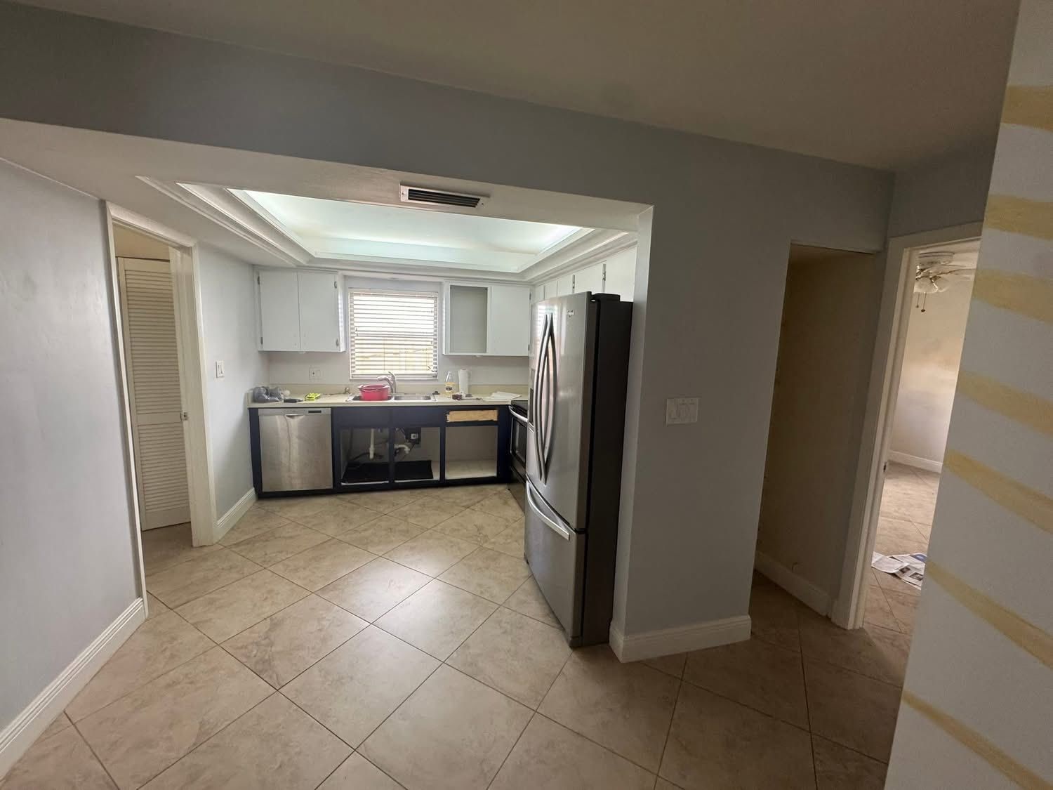 Kitchen interior with cabinets, refrigerator, and doorway to the hallway. Tile floor and neutral wall colors.