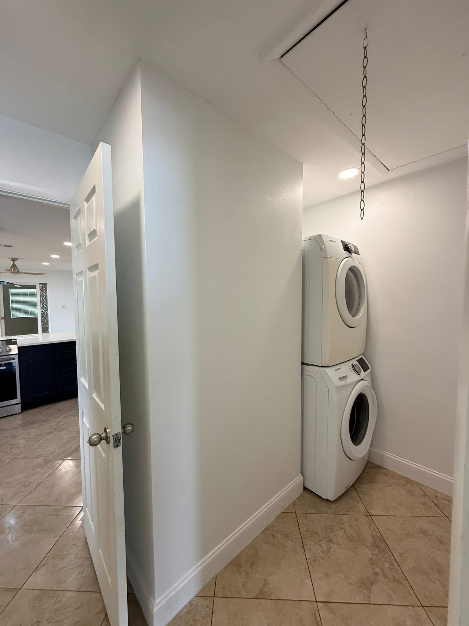 Hallway with a stacked washer and dryer unit, white door, and tile flooring.