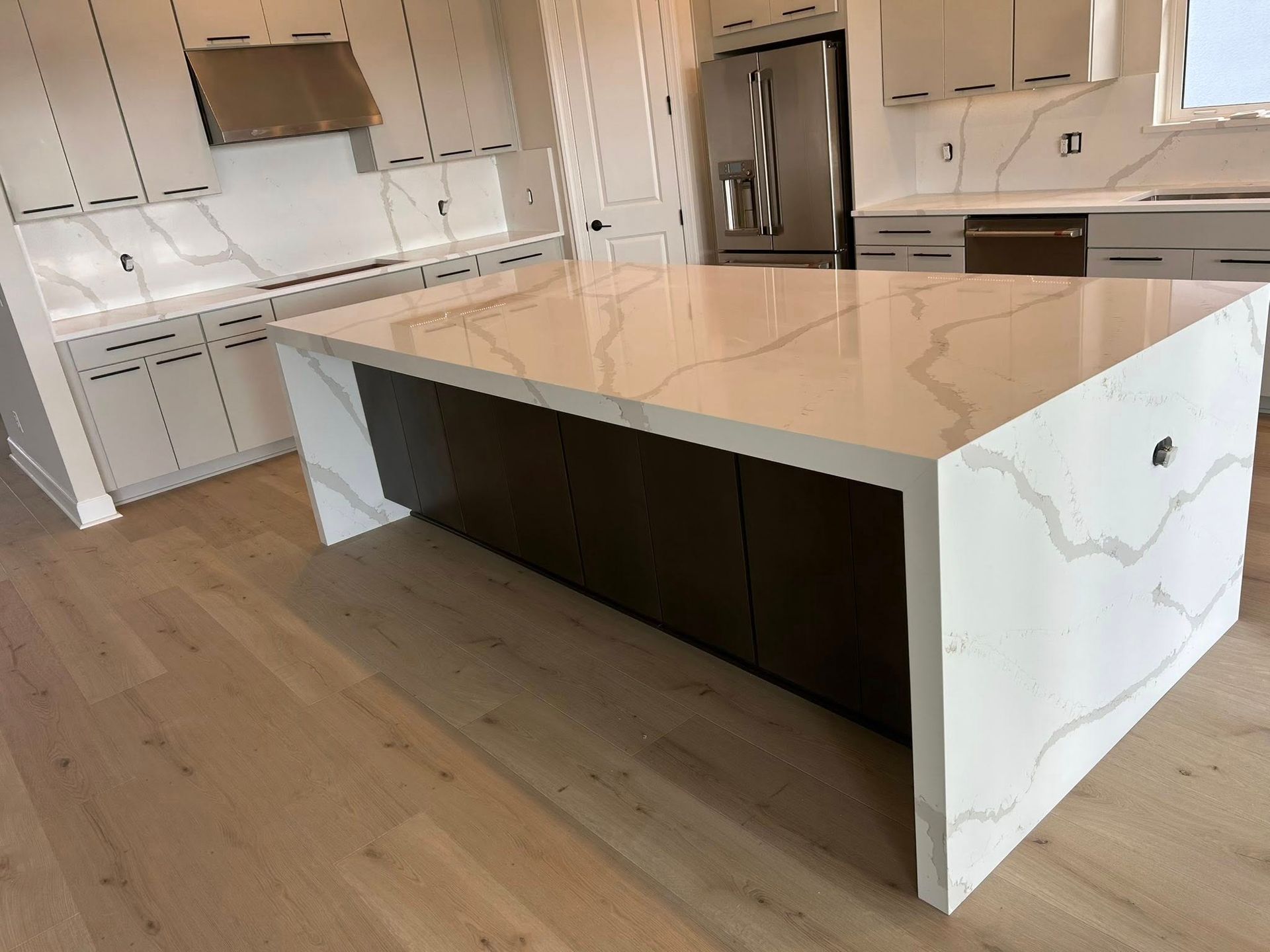 Kitchen with a large island with white countertops, dark cabinets and light wooden floors.