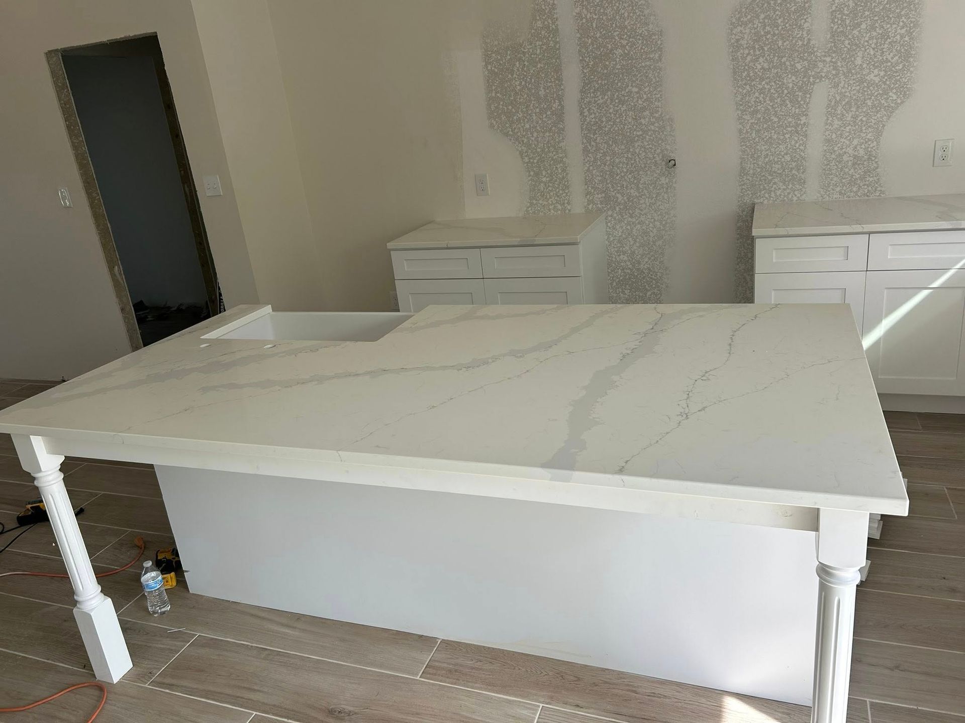 White kitchen island with marble countertop, cabinets, unfinished walls, and wooden floors.