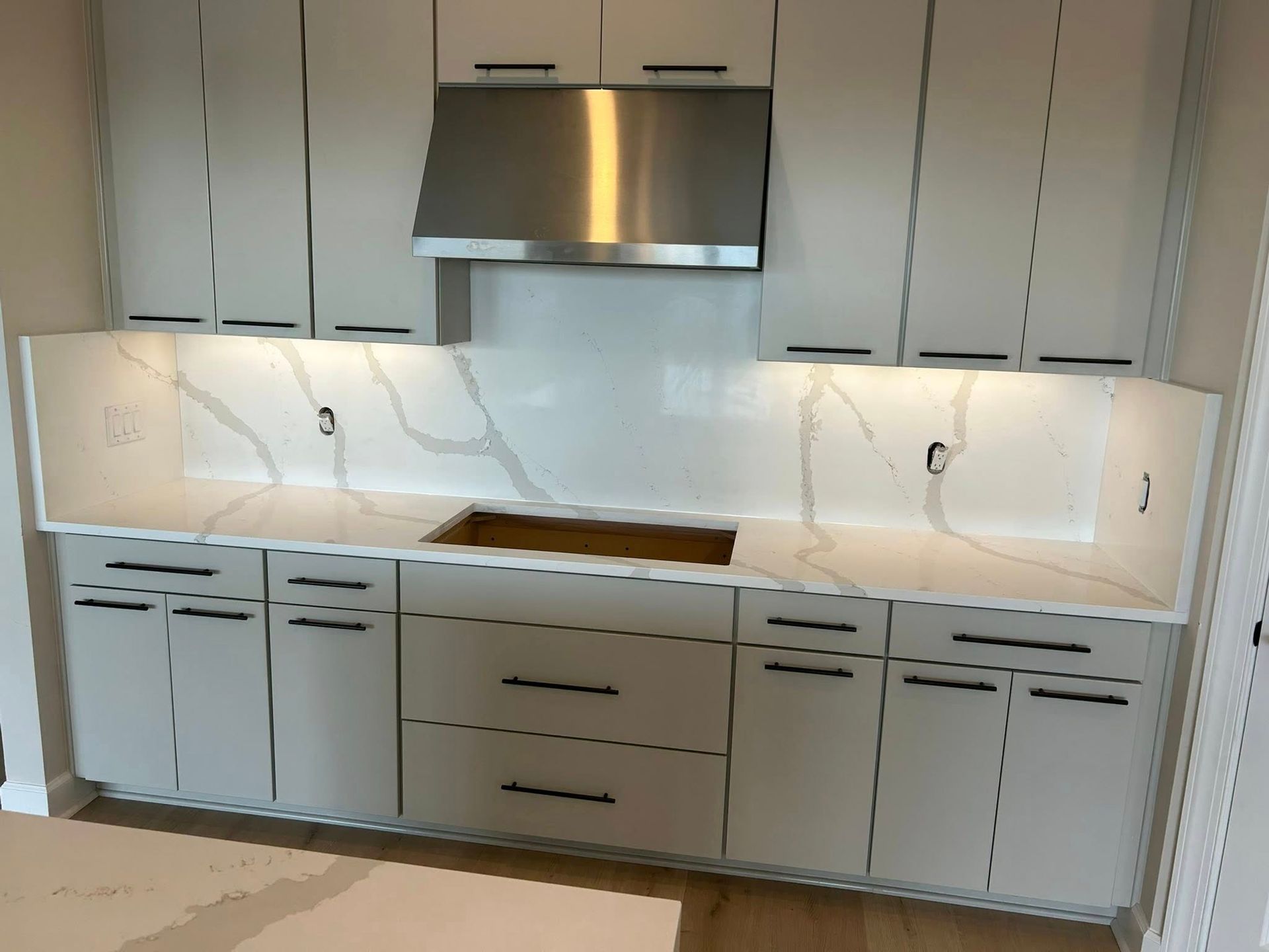 White kitchen cabinets with stainless steel range hood and marble countertop.