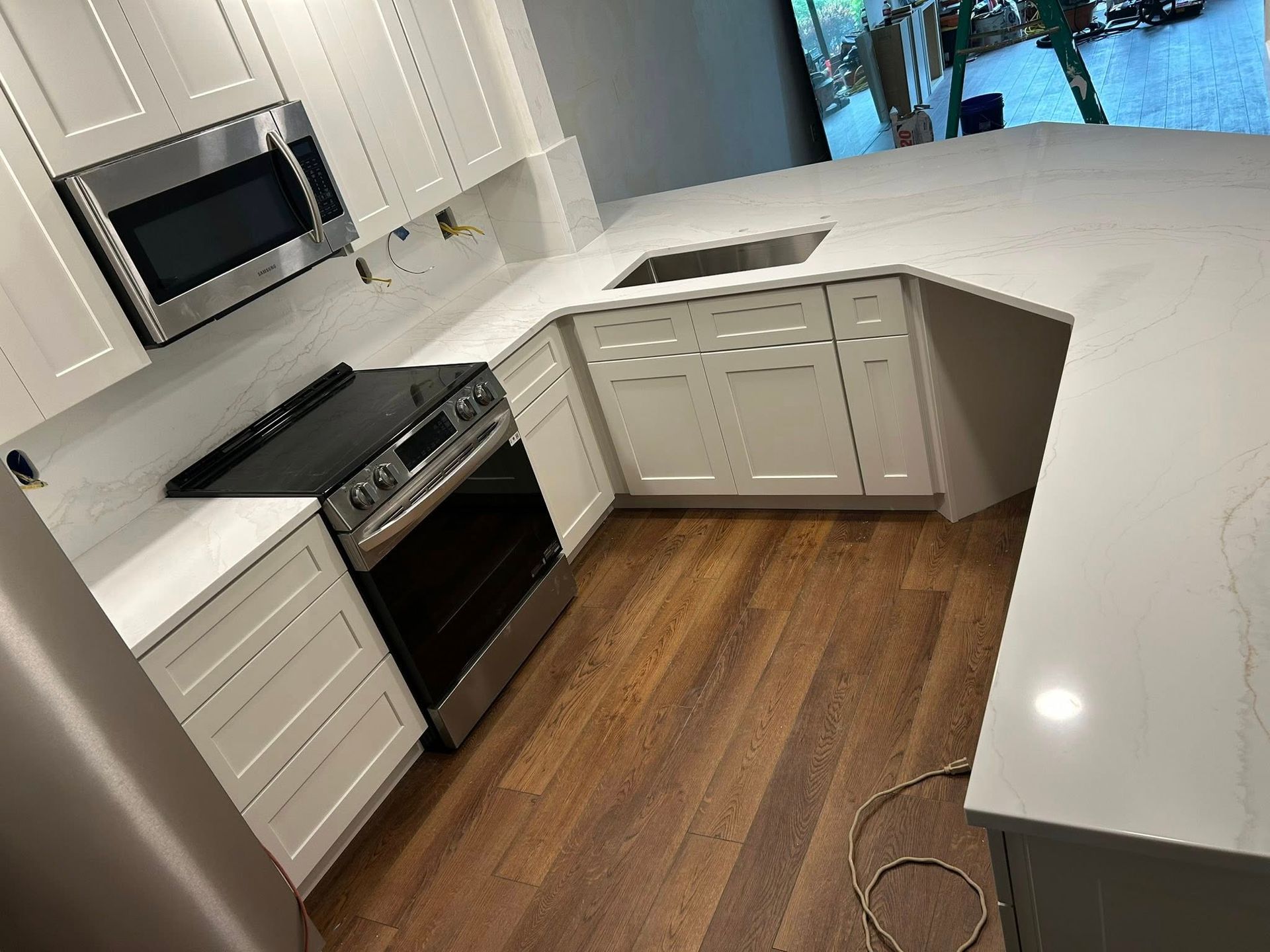 U-shaped kitchen with white cabinets, light countertops, stainless steel appliances, and wood flooring.