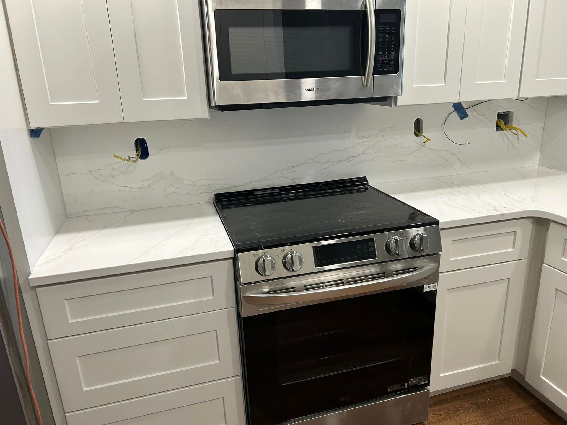 White kitchen with a stainless steel microwave and oven, installed between white cabinets and countertops.