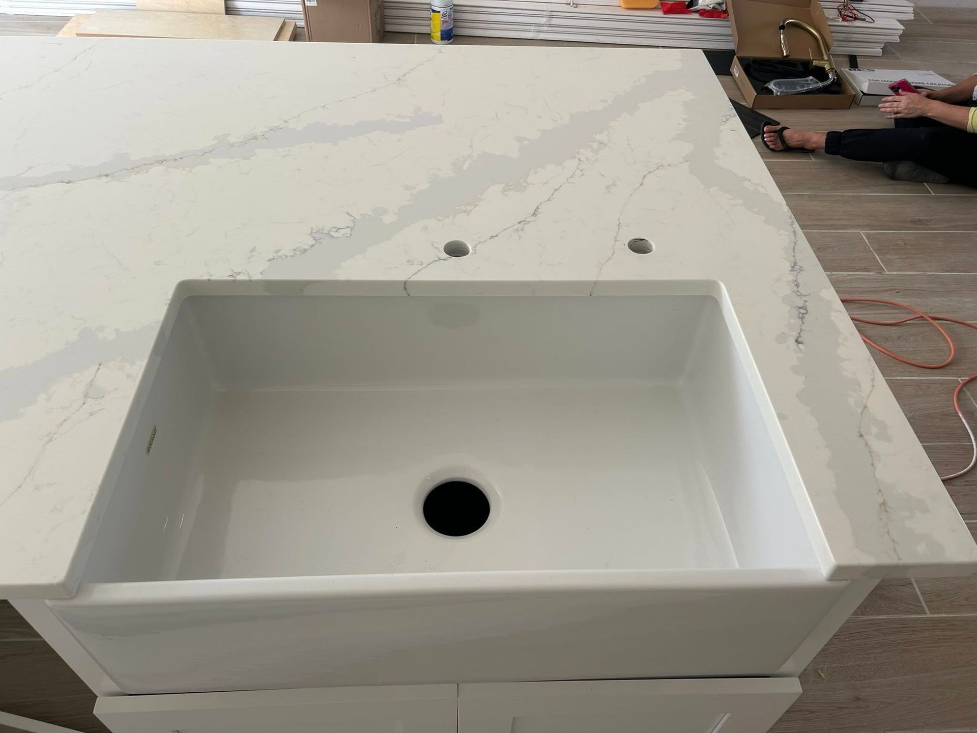 White kitchen sink installed in a white quartz countertop, with two faucet holes visible.