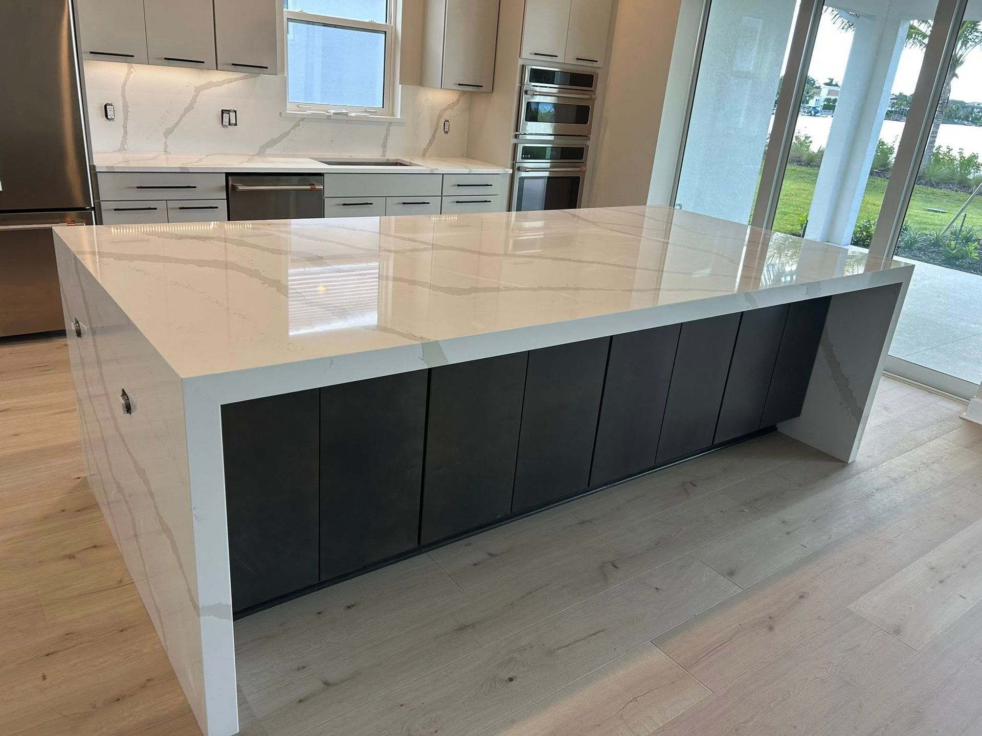 Modern kitchen with large white island, dark gray cabinets, and light wood flooring.