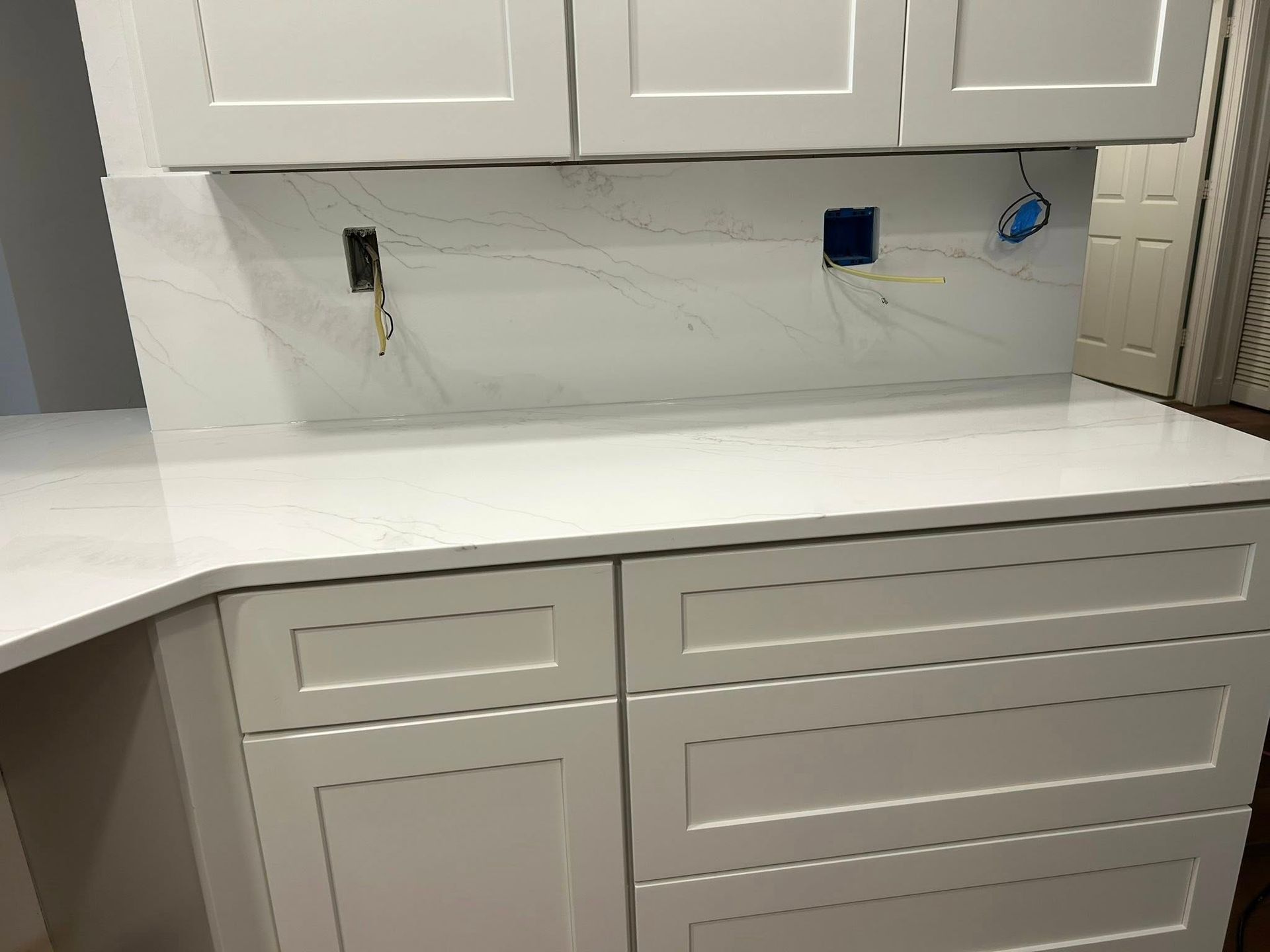 White kitchen cabinets and countertops with marble backsplash. Electrical outlet boxes are present.