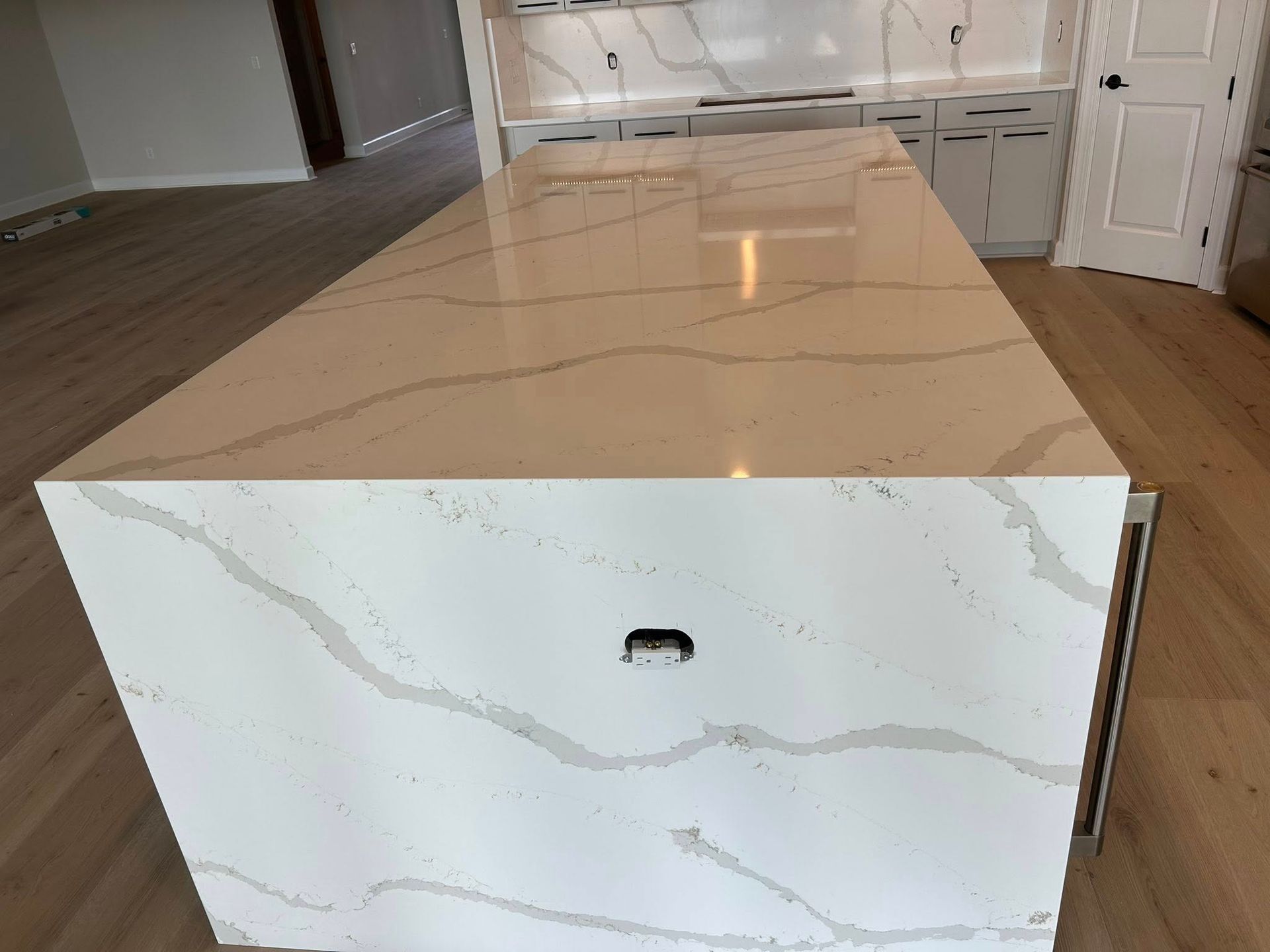 Kitchen island with white quartz countertop and cabinets, light wood floor.