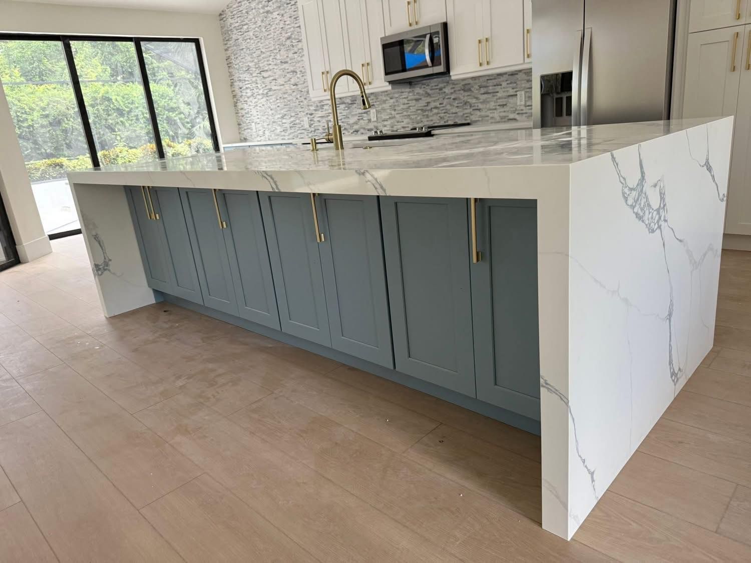 Modern kitchen island with marble-look countertop and blue cabinets, gold hardware, and light wood floor.