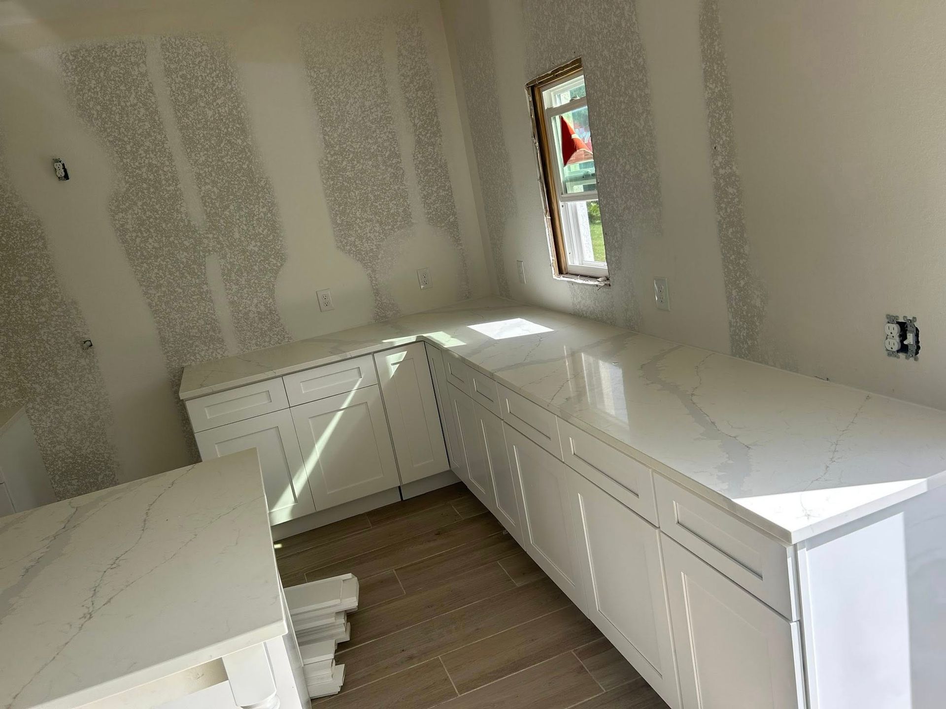Kitchen under construction with white cabinets, countertops, and a small window.
