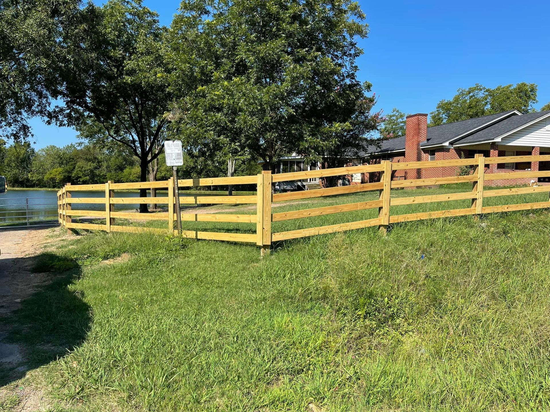 A wooden fence surrounds a grassy field in front of a house.