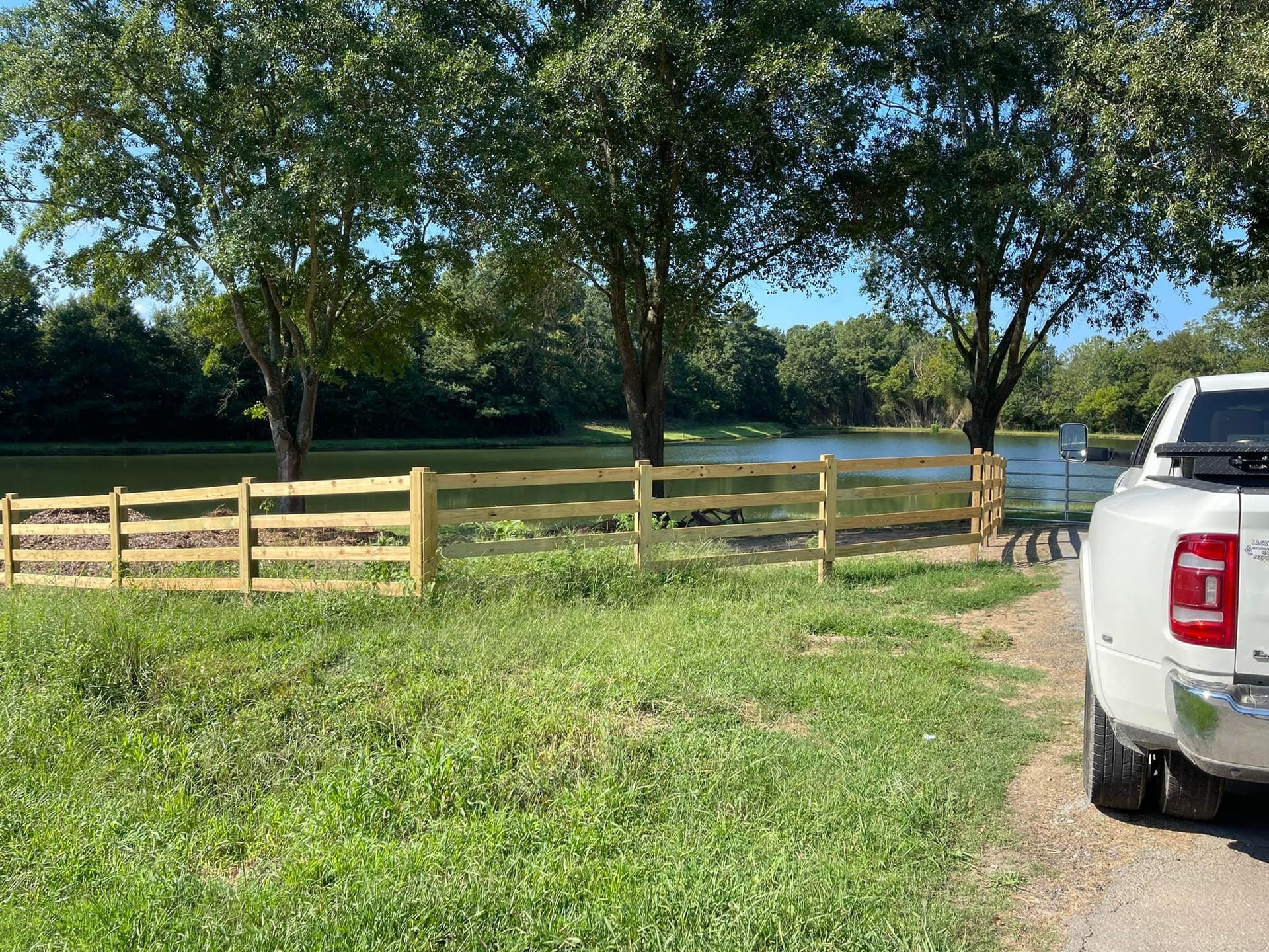 A white truck is parked in a grassy field next to a wooden fence.