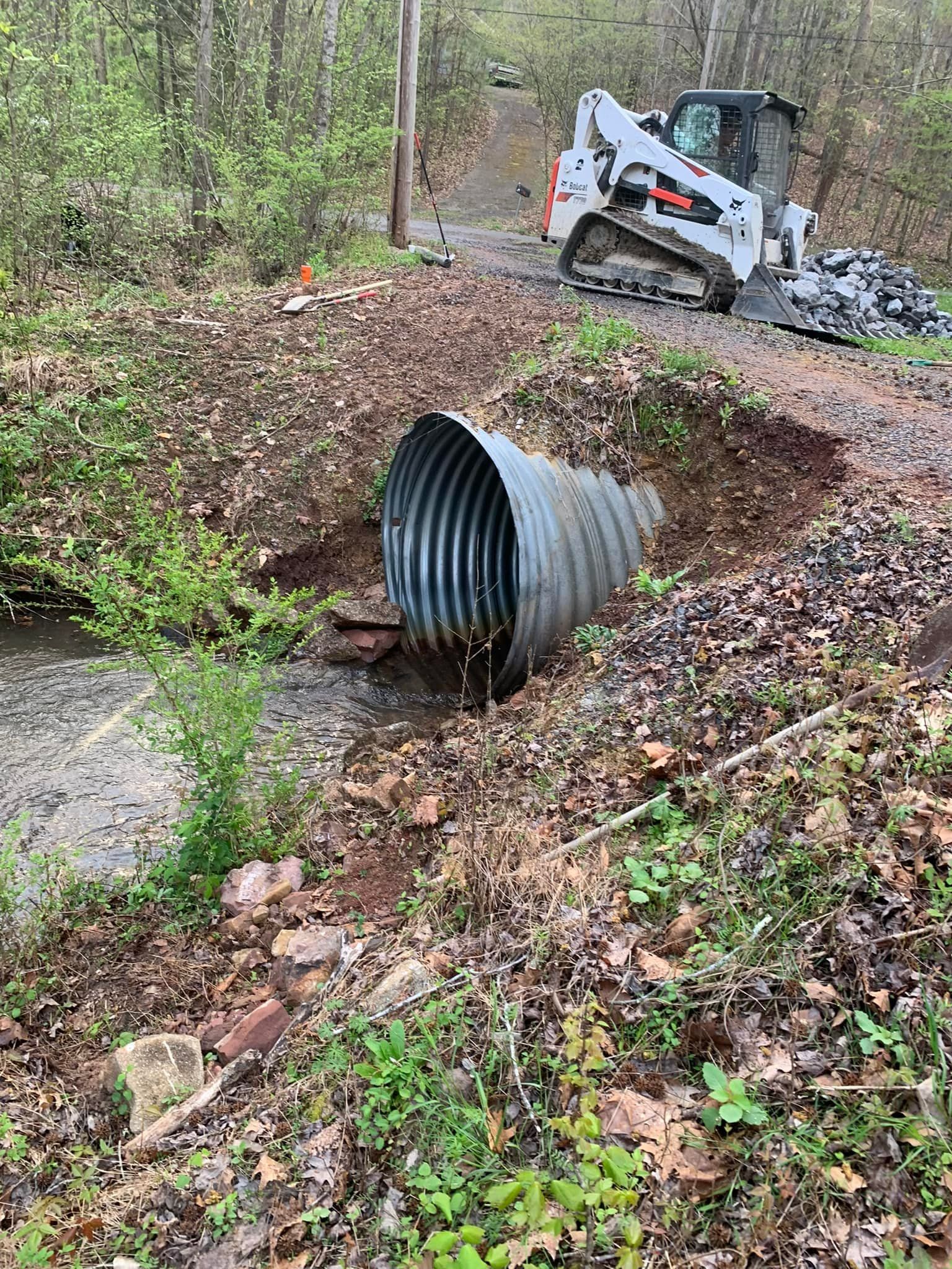 A bulldozer is driving down a dirt road next to a metal pipe.