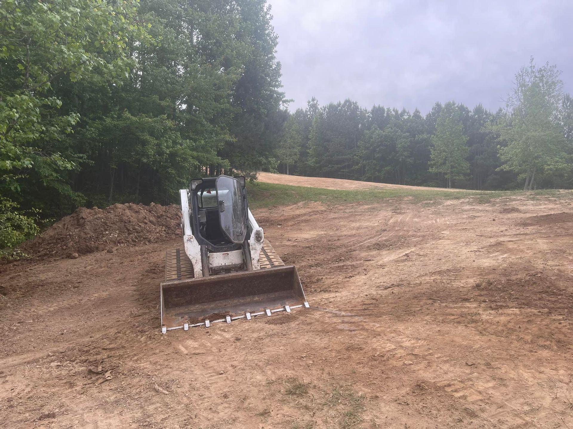 A bulldozer is moving dirt in a field with trees in the background.