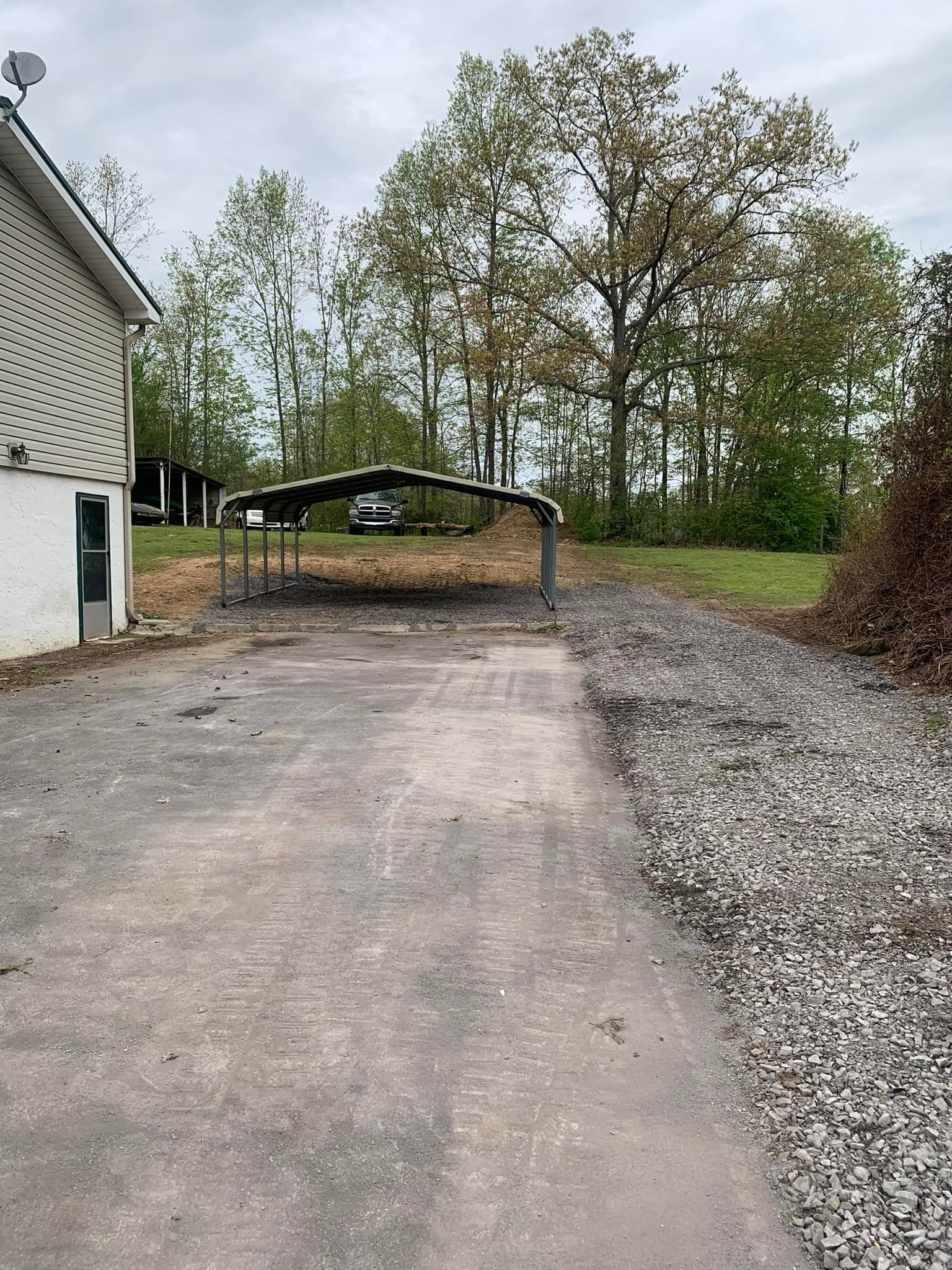 A gravel road leading to a house with a carport in the background.