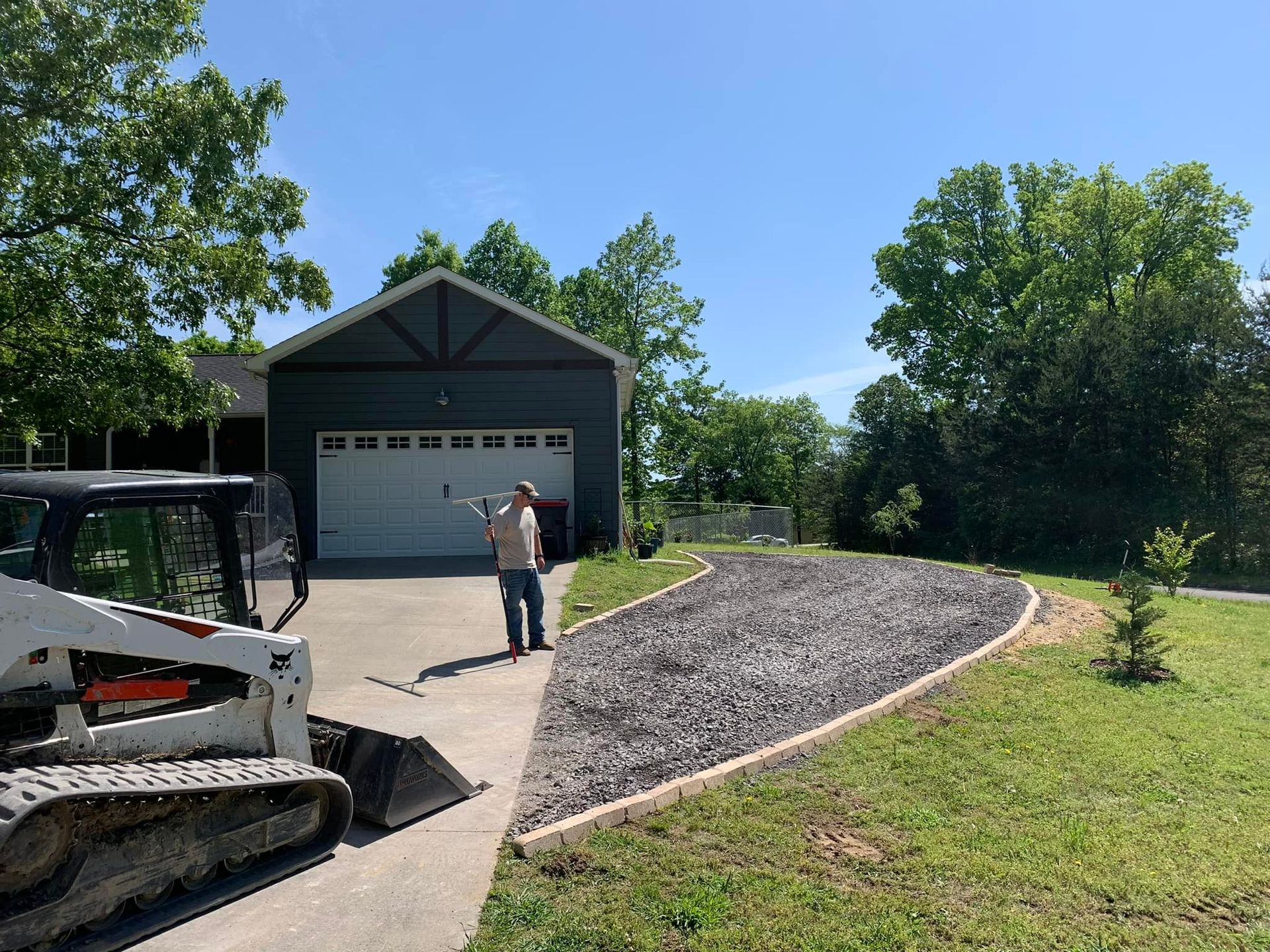 A man is standing in front of a garage next to a bulldozer.
