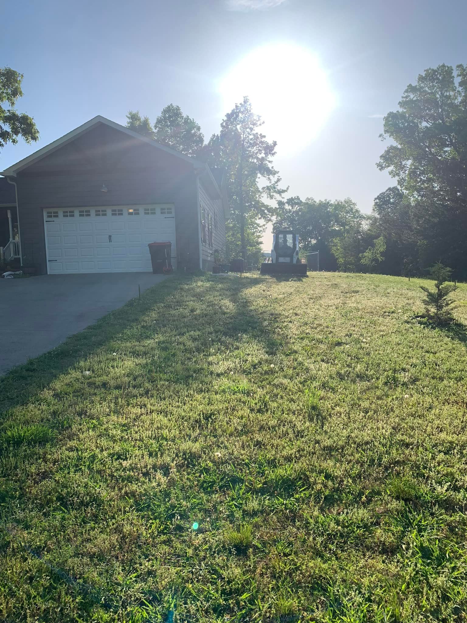 The sun is shining brightly on a lush green lawn in front of a house.