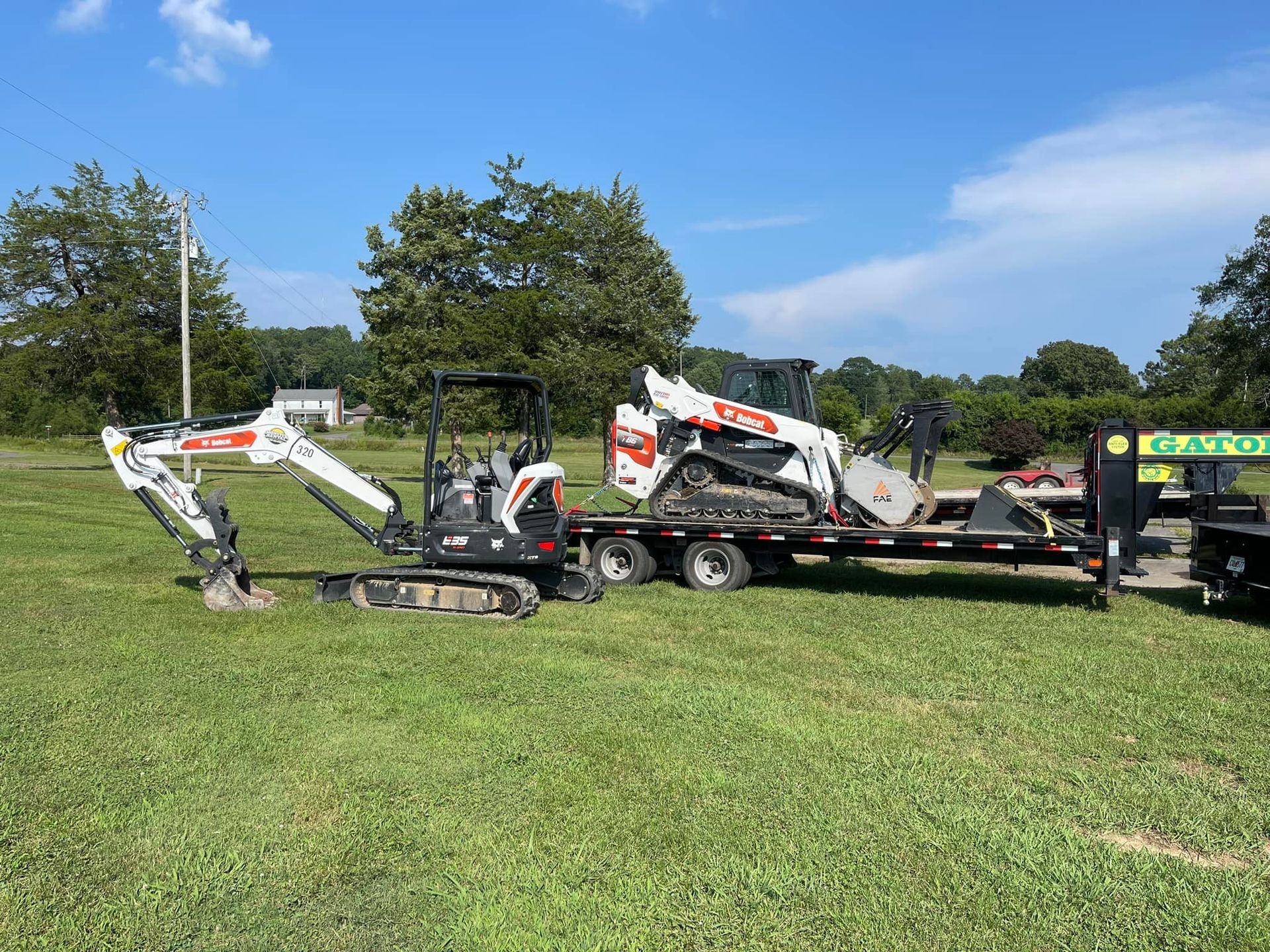 A small excavator is sitting on top of a trailer in a grassy field.