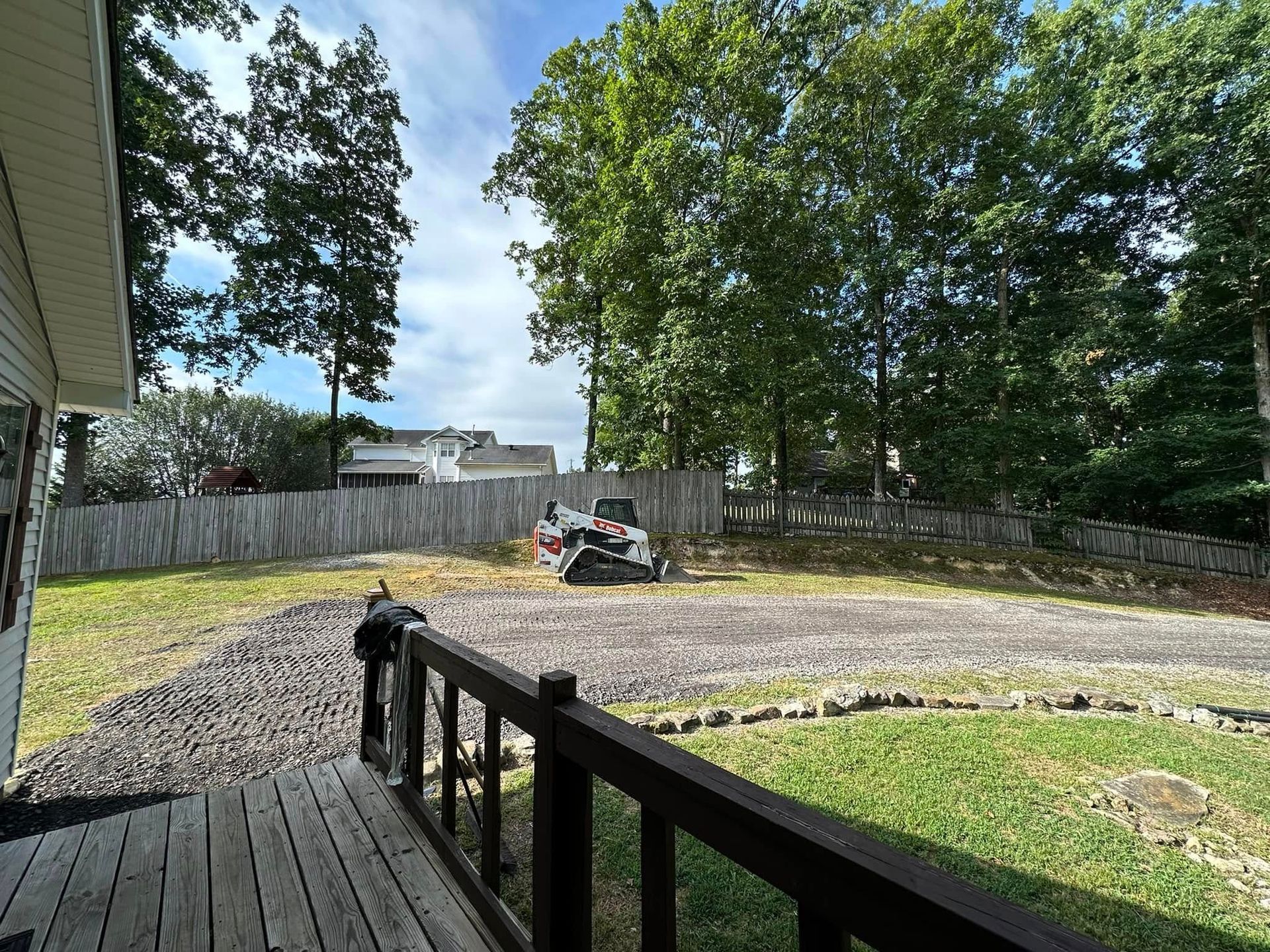 A view of a backyard from a deck with a fence and trees in the background.