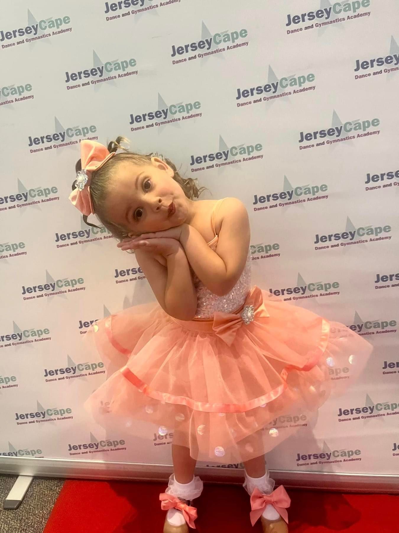 Young child in a pink tutu posing with hands on cheeks at a Jersey Cape backdrop