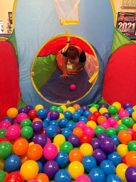Child crawling through a colorful play tunnel into a ball pit filled with bright plastic balls