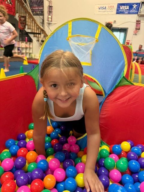 Child crawling through a colorful ball pit toward a blue tunnel at an indoor play area