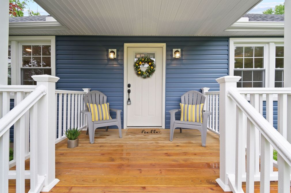 Blue house front porch with two gray chairs, white railing, and a welcoming wreath on the door.