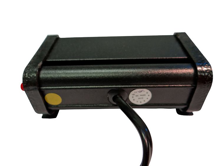 Black electronic device with power cord, a red LED, and two stickers, presumably on a desk.