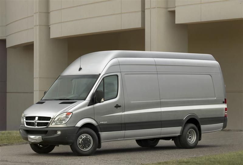Silver Dodge Sprinter van parked in front of a beige building.