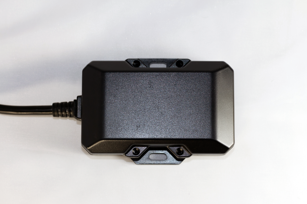 Black rectangular electronic device with a cable attached, against a white backdrop.