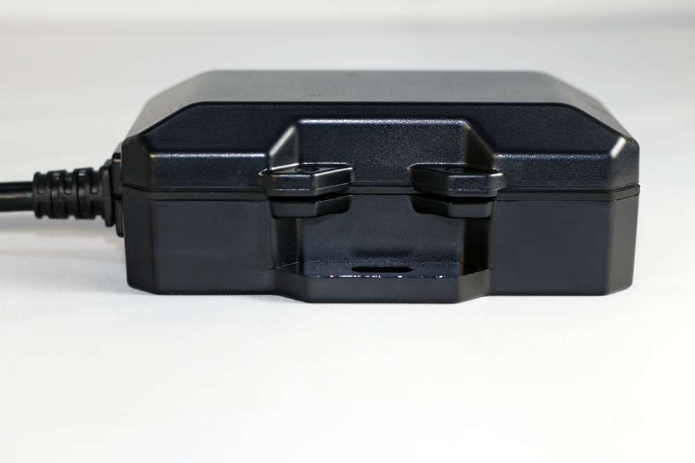 Black, rectangular, electronic device with a connected cable; sitting on a white surface.