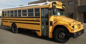 Yellow school bus parked in front of a building, door open.