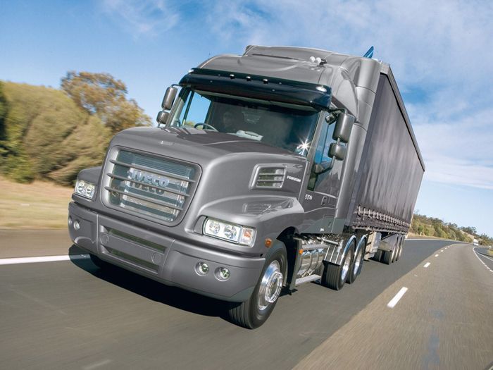 Gray semi-truck with trailer speeding down a highway on a sunny day.