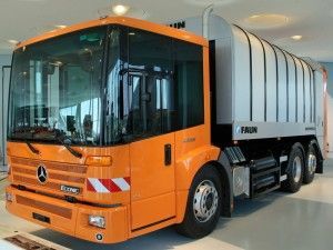 Orange and silver garbage truck; parked indoors, angled view. Mercedes-Benz logo visible.