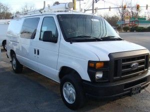 White Ford work van with a ladder rack, parked on a street.