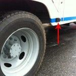 Black button on a white truck near a tire; an arrow points to the button.