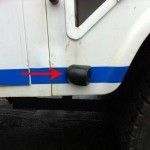 White vehicle side with blue stripe and black bumper. Red arrow points left.