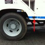 Close-up of a large white truck's tire, with a black side marker light indicated by a red arrow.