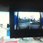 Rear-view camera monitor displaying three views of a street from inside a vehicle.