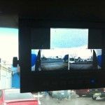 Screen showing split views of a cloudy sky and parked vehicles, mounted in a vehicle interior.