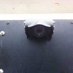 Black camera mounted on a dark surface with silver screws, against a light-colored background.