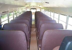 Interior of an empty school bus with rows of brown seats and a central aisle.