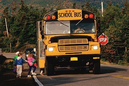 Yellow school bus stopped with children boarding on a road; stop sign displayed.
