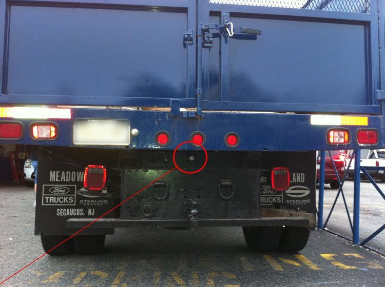 Rear view of a blue truck with black bumper. Red lights and a hitch are visible. The setting is an outdoor area.