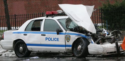A wrecked police car with a crushed front, in an urban setting.