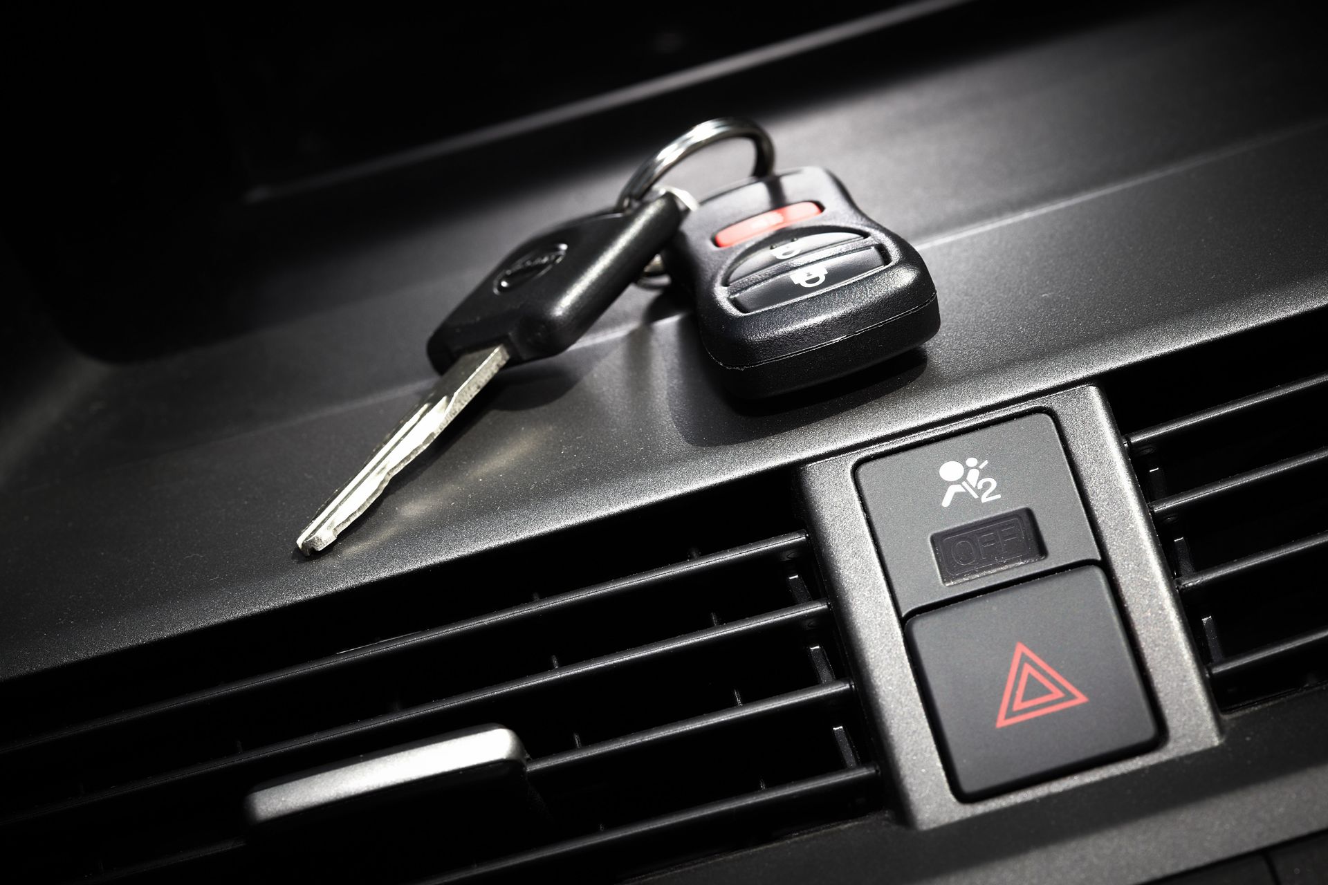 Car keys resting on a car dashboard near the air vent and hazard light button.