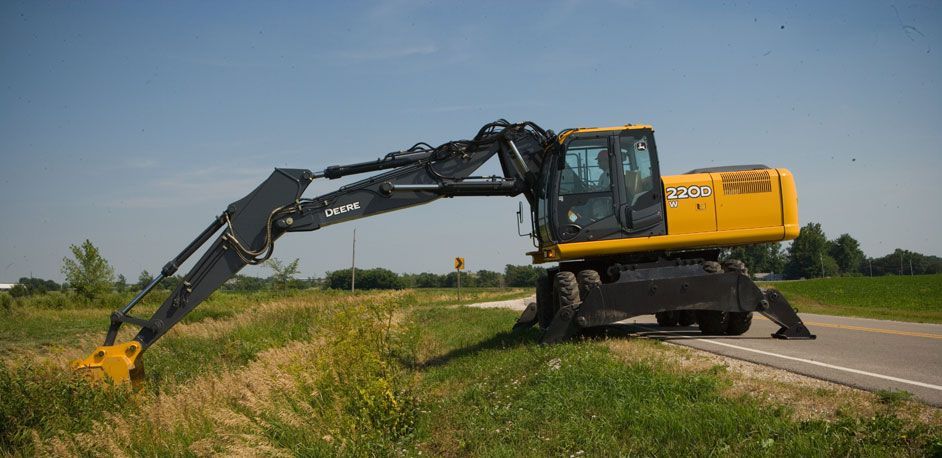 Yellow excavator mowing roadside grass on a sunny day.