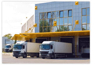 Trucks at loading docks of a modern warehouse, yellow awnings and metal facade.