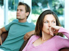 Woman and man sitting indoors, looking away. Woman has hand near face, looking thoughtful.