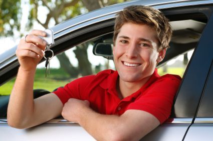 Smiling young man in a red shirt holding car keys, sitting in a car.