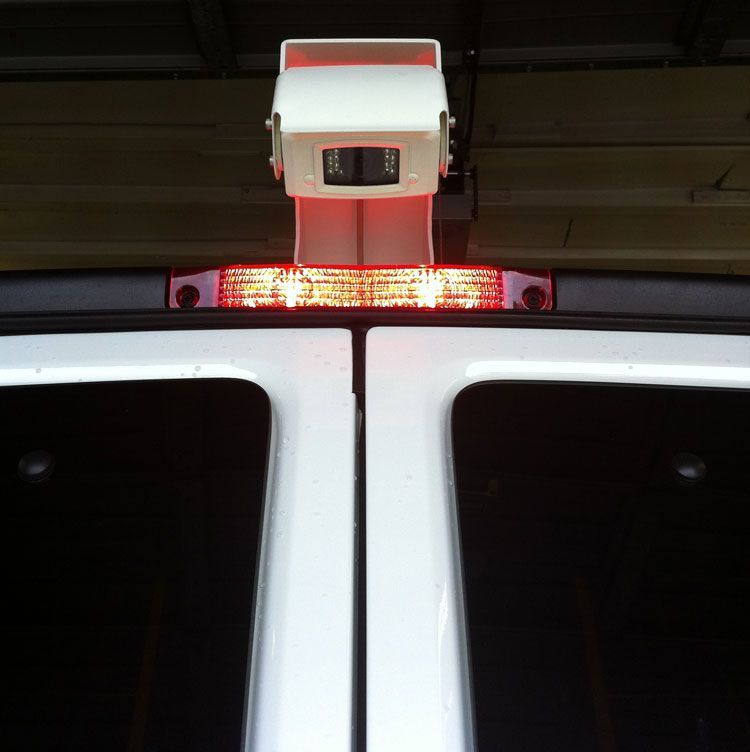 White van rear with camera and flashing red light bar.